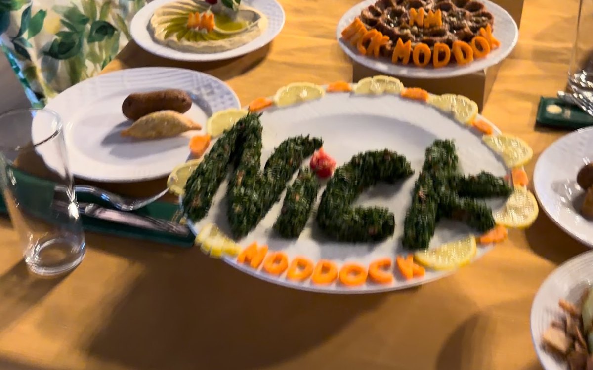 A table full of Syrian dishes, with one platter that spells Nick in green herbs