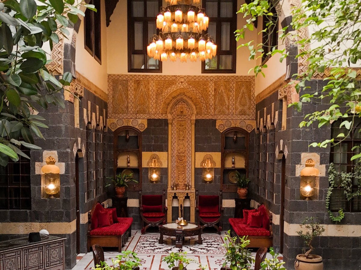 The courtyard of a restored palace hotel in Old Damascus, with a chandelier and red velvet chairs