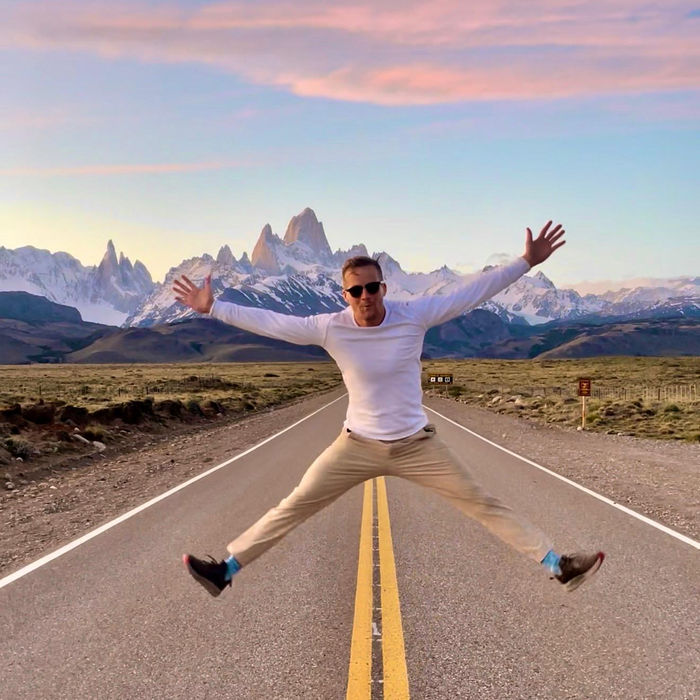 Nick jumping in the middle of an empty road, with snowy mountain peaks behind him