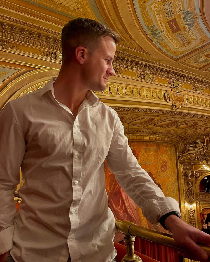 Nick Maddock in a white shirt on the balcony of a grand old theatre