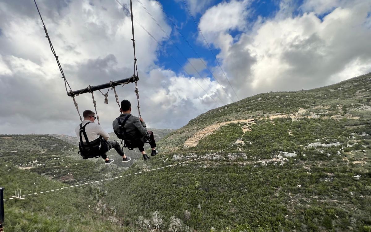 Two people on a giant swing above the green hills near Tartus